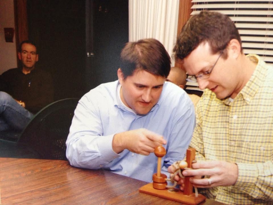 Cory Cox working through a problem with a colleague while Governor Mike Huckabee looks on
