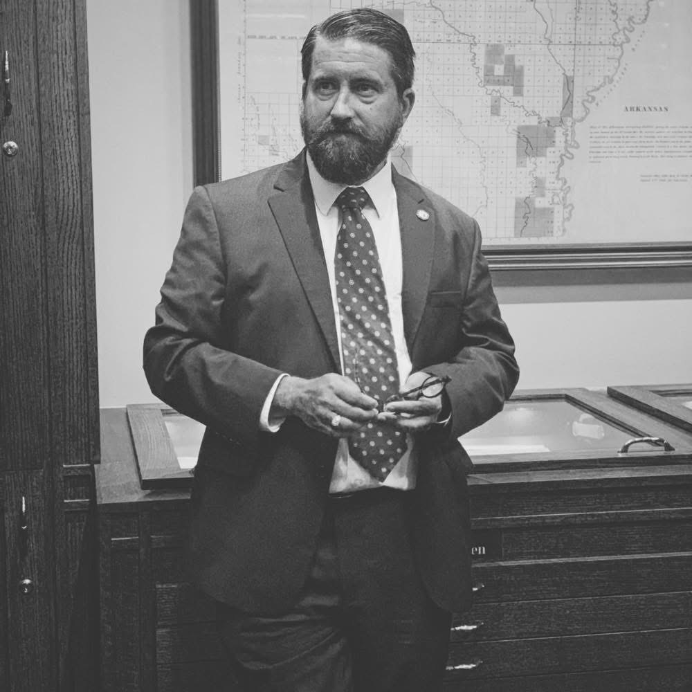 Cory Cox photographed in black and white in front of a historical map of Arkansas